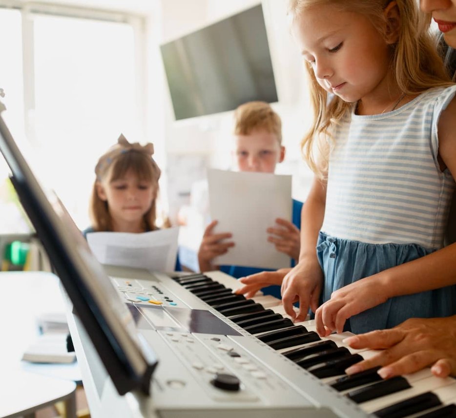 Adult helping child play keyboard with other children watching