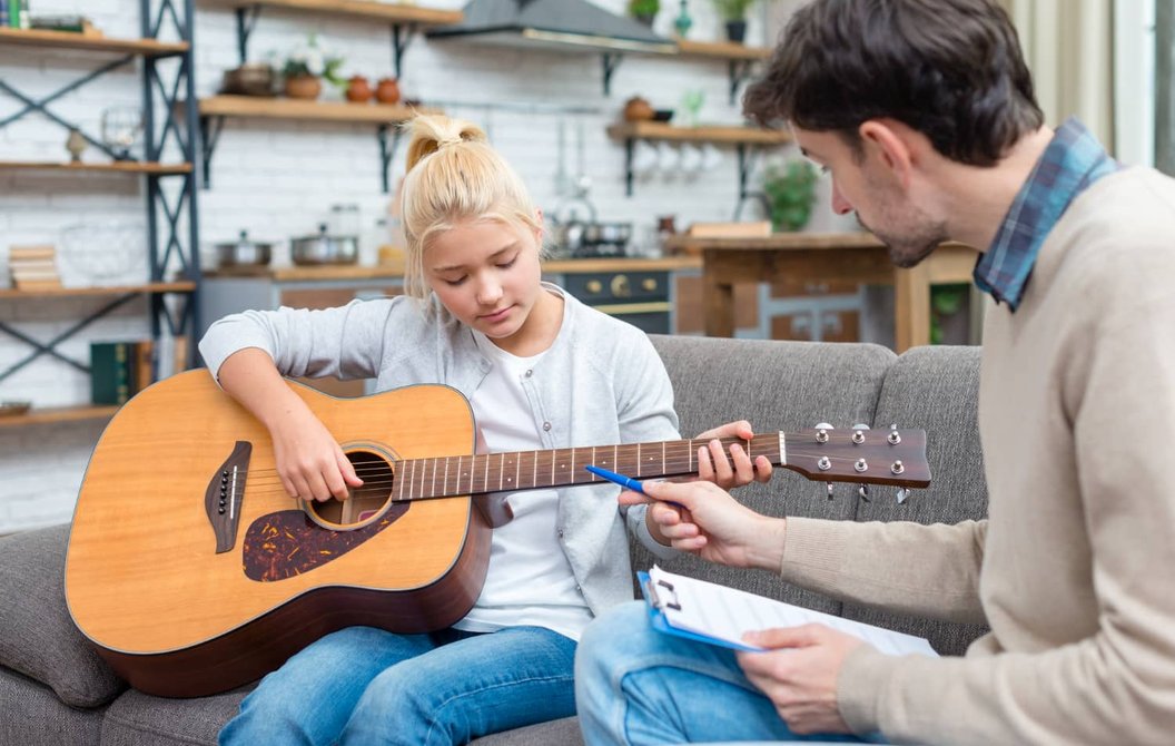 Man teaching teen girl guitar on couch at home
