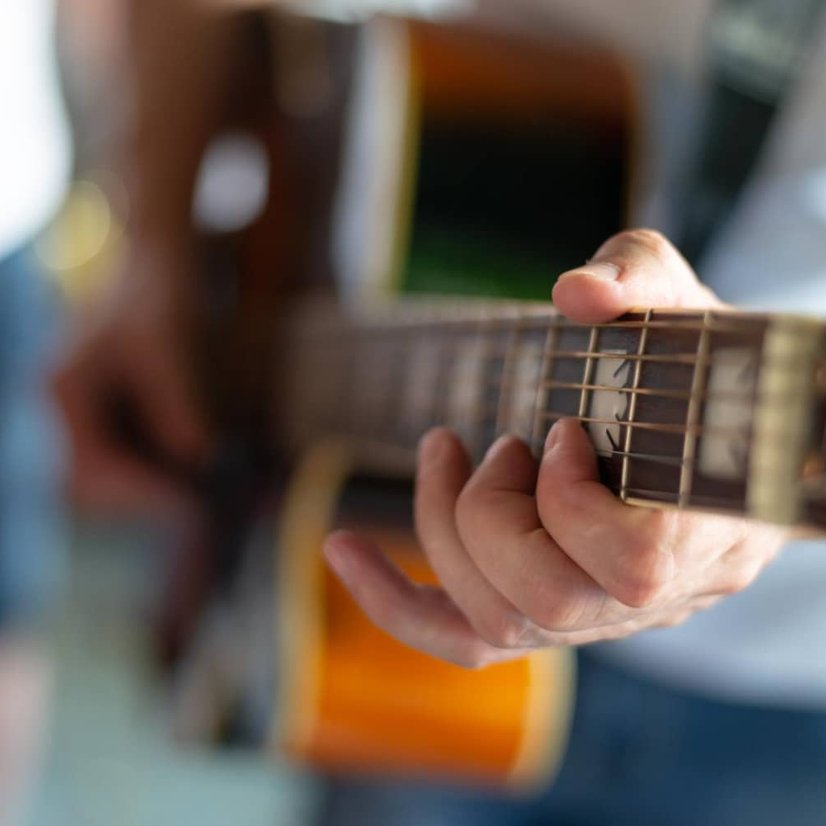 Close-up of hands playing chords on acoustic guitar fretboard