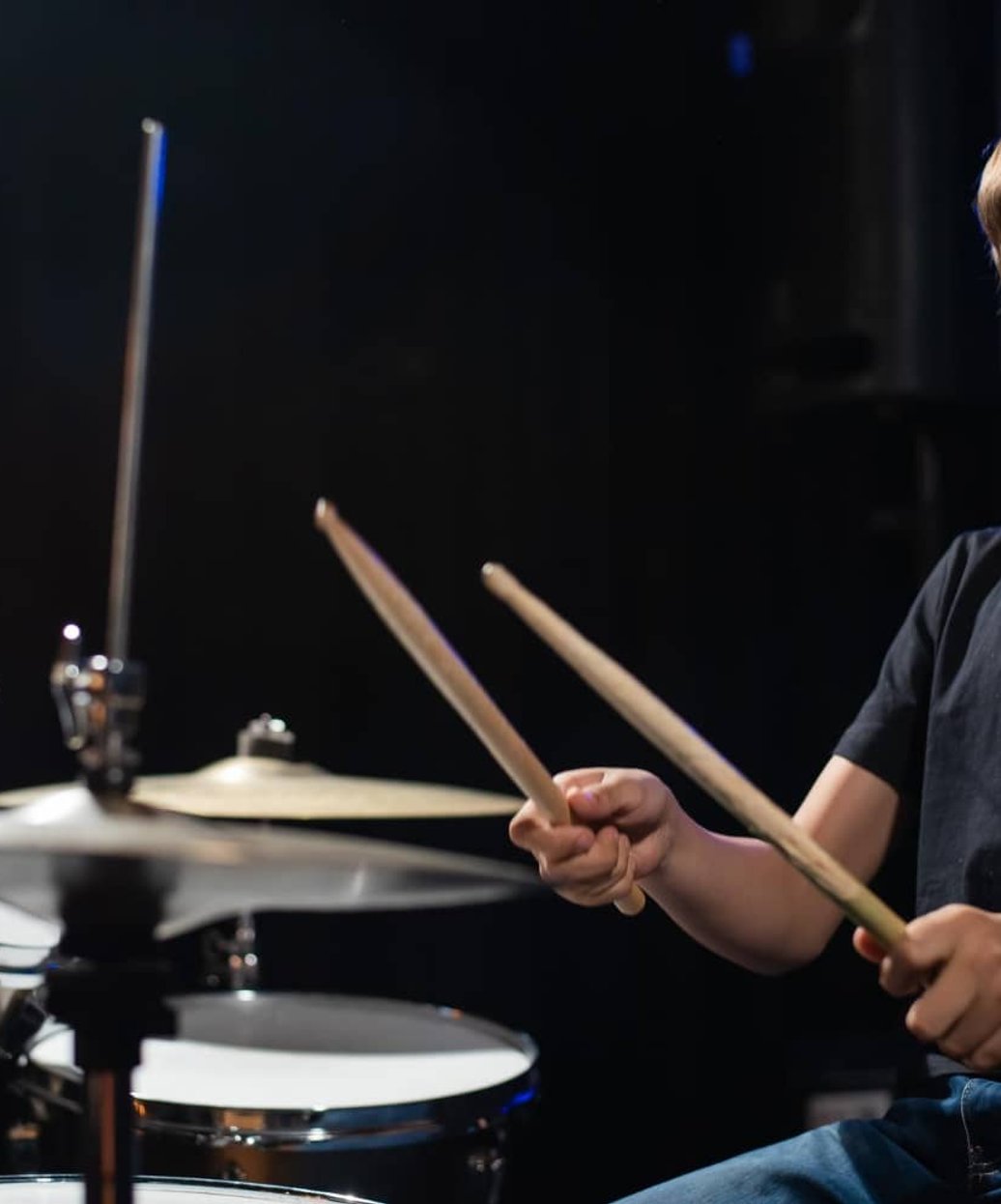 Smiling boy playing drum set with drumsticks in studio