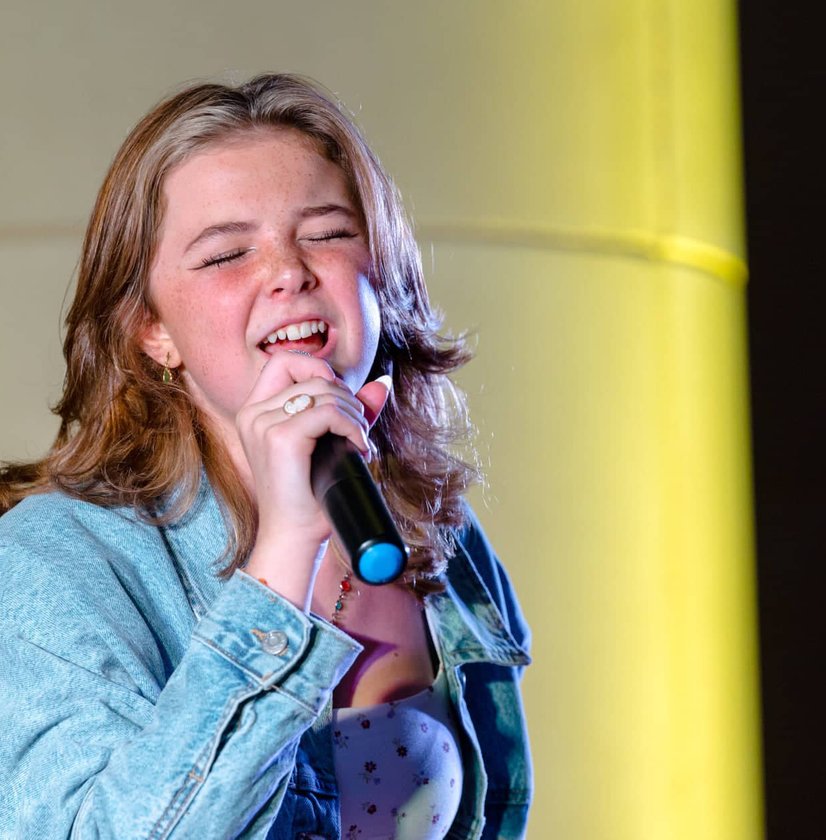 Teen girl singing into microphone with denim jacket on